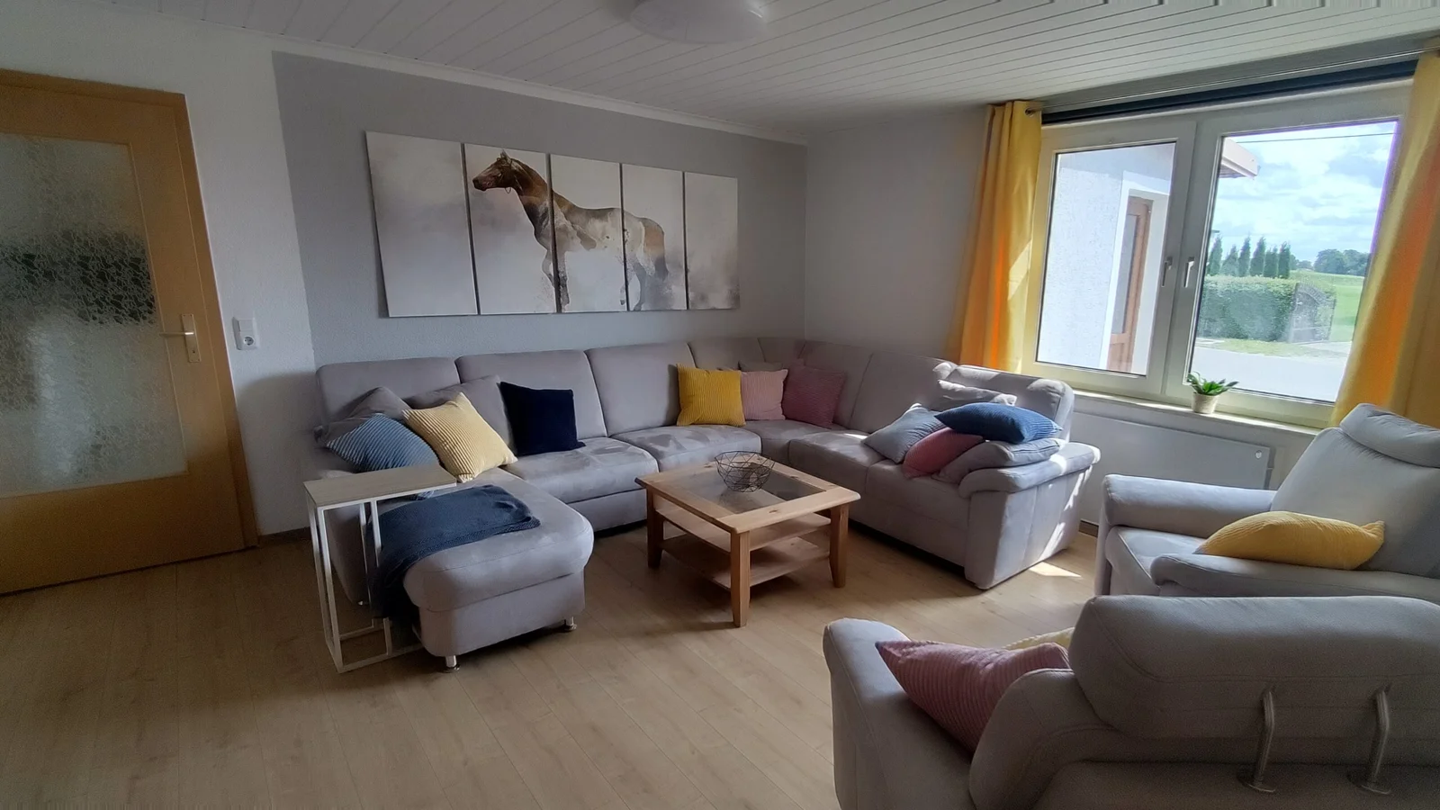 Heller Wohnbereich mit Sofa, Sesseln und großem Fenster